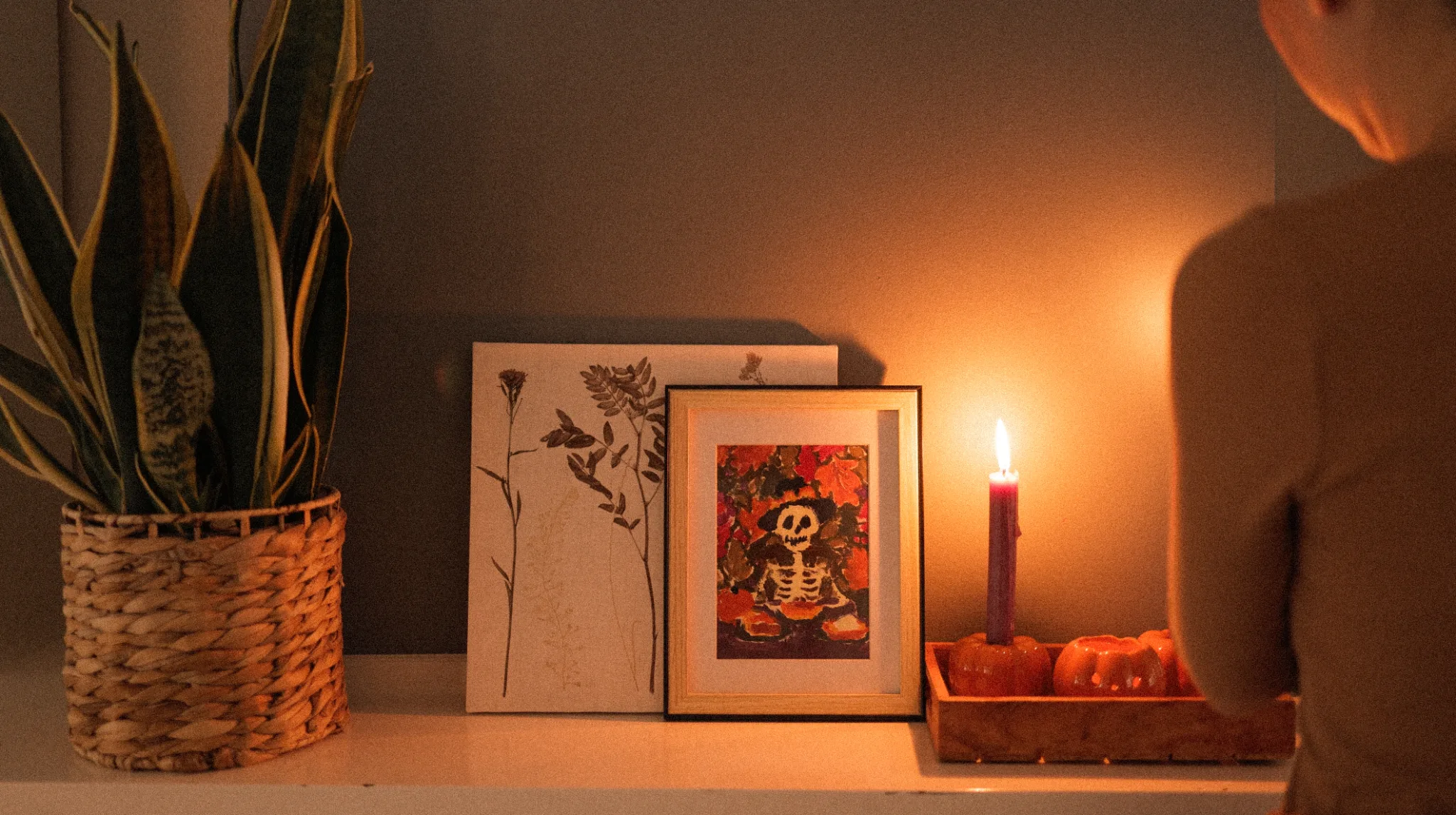 Cozy fall mantel with candlelight Candlelit fall mantel with a framed skeleton painting, pressed leaves on canvas, pumpkin candle holders, and a snake plant.